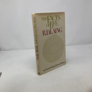 May include: A white book with a red title "The Facts of Life" by R.D. Laing. The book cover features a circular design and the text "An Essay in Feelings Facts, and Fantasy".