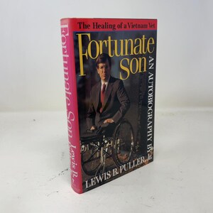 May include: A hardcover book titled Fortunate Son: The Healing of a Vietnam Vet, an autobiography by Lewis B. Puller, Jr. The cover features a photograph of a person in a dark suit sitting in a wheelchair, with yellow and white text.