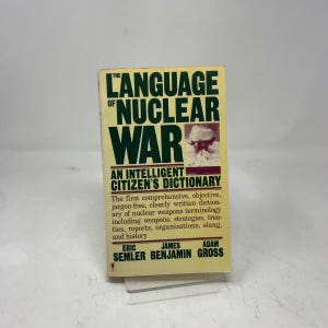 May include: A book titled "The Language of Nuclear War: An Intelligent Citizen's Dictionary." The cover is yellow with bold green and white text. The book includes a photo of a mushroom cloud.