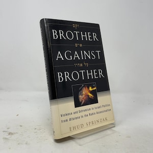 以下が含まれることがあります： エフード・スプリンザック著『Brother Against Brother』のハードカバー本。黒い表紙には白い文字、ヘブライ語の文字、そして炎を持つ人物が写る中央の正方形の画像が配置されている。下部はクリーム色で、黒い文字が印刷されている。