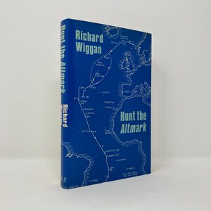Puede incluir: Una cubierta de libro azul con un mapa del Océano Atlántico Norte y el texto "Hunt the Altmark" en blanco. El nombre del autor, Richard Wiggan, está impreso en blanco en la cubierta.