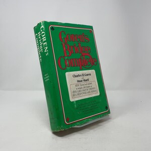 May include: A green book titled "Goren's Bridge Complete" with red and white text. The book features a diamond, club, and spade symbol on the cover. The book is a guide to bridge.