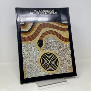 Puede incluir: Una portada de libro con fondo negro y un diseño de arte aborigen colorido que presenta una serpiente y un círculo. El título del libro es "Mr. Sandman Bring Me A Dream".