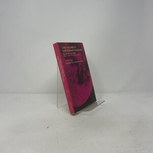 May include: A book titled "Celestial Objects for Common Telescopes" is displayed on a clear stand. The cover is a vibrant pink with the title in white and a dark illustration. The book is Volume One: The Sun & Shadow.