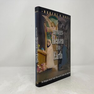 May include: A book titled "Between Heaven and Earth: The Religious Worlds People Make and the Scholars Who Study Them" by Robert A. Orsi. The cover features a painting of a woman in a white dress and a halo, standing in front of a golden door.