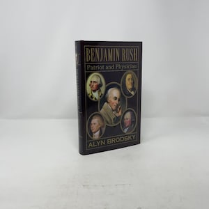May include: A hardback book titled "BENJAMIN RUSH Patriot and Physician" by Alyn Brodsky. The cover is dark brown with portraits of historical figures. The book is standing upright against a white background.