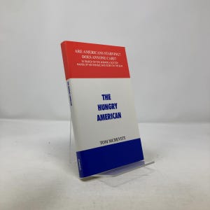 Può includere: Un libro intitolato "The Hungry American" di Tom McDevitt. La copertina è bianca con sezioni blu e rosse. Il titolo è in grandi lettere blu. La copertina include anche il testo "Are Americans Starving? Does Anyone Care?"