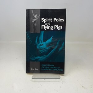 May include: A book titled "Spirit Poles and Flying Pigs" with a teal and black cover. The cover features an illustration of a winged figure and a creature with horns. The book's subtitle reads "Public Art and Cultural Democracy in American Communities."