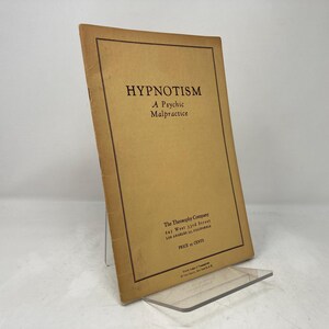 Puede incluir: Un libro de color beige con el título "Hypnotism: A Psychic Malpractice" impreso en letras rojas oscuras. El libro es publicado por The Theosophy Company, 141 West 32nd Street, Los Angeles, California. El precio es de 11 centavos.