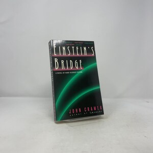 Puede incluir: Un libro de tapa dura titulado "Einstein's Bridge: A Novel of Hard Science Fiction" de John Cramer. La portada es negra con dos líneas verdes curvas y el título en letras blancas y rosas.