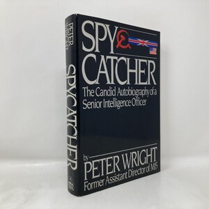 May include: A hardcover book titled "SPY CATCHER" by Peter Wright. The book has a dark blue cover with white lettering and a red hammer and sickle symbol with the British and American flags. The book's spine also features the title.