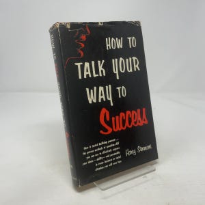 May include: A vintage book titled "How to Talk Your Way to Success" with a black cover and white and red lettering. The book has a graphic of a face on the upper left corner. The author's name is Harry Simmons.