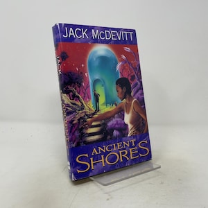 May include: A hardcover book titled Ancient Shores by Jack McDevitt. The cover features a science fiction illustration with a person reaching toward a glowing blue dome structure in a purple landscape, with the title in large yellow lettering.