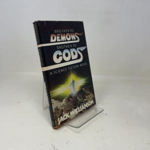 Könnte beinhalten: Ein Science-Fiction-Roman aus der Zeit mit dem Titel "Brother to Demons, Brother to Gods" von Jack Williamson. Das Buch hat einen dunklen Einband mit dem Titel in Weiß und Rot und eine futuristische Illustration.