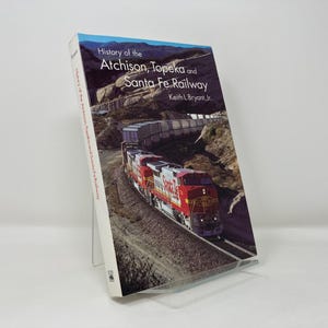 May include: A book titled "History of the Atchison, Topeka and Santa Fe Railway" by Keith L. Bryant, Jr. The cover features a red and silver train engine traveling through a mountainous landscape.
