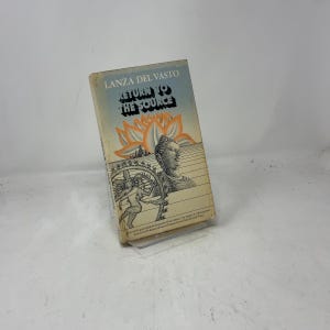 May include: A paperback book titled "Return to the Source" by Lanza Del Vasto. The cover features a lotus flower, a Buddha head, and an illustration of a figure with a wheel. The book has a light blue and orange color scheme.