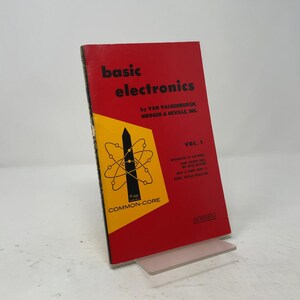 May include: A red and yellow softcover book titled Basic Electronics by Van Valkenburgh, Nooger & Neville, Inc. Vol. 1. The cover features a black atom graphic, the text Common-Core, and a list of topics including vacuum tubes and power supplies.
