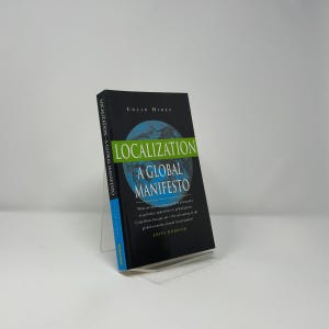 May include: A hardcover book titled "Localization A Global Manifesto" by Colin Hines. The book has a black cover with the title in large green and white text, and a blue and white globe graphic. The book is displayed on a clear acrylic stand.