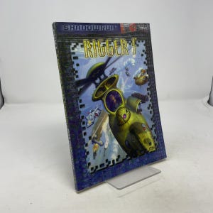 May include: A vintage "Shadowrun Rigger 3" role-playing game book. The cover features a futuristic scene with a yellow vehicle, figures, and the title in a bold, stylized font. The book is displayed on a clear plastic stand.