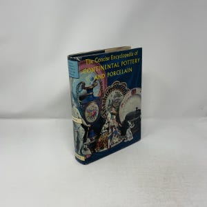 May include: A hardcover book titled The Concise Encyclopedia of Continental Pottery and Porcelain. The dark blue dust jacket features a collage of colorful ceramic vases, ornate plates, and figurines, with yellow text on the front cover.