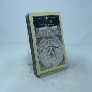 May include: A paperback book titled Plotinus The Enneads from Penguin Classics. The cover is cream-colored with a black rectangular header containing white text. A central black and white illustration depicts a human figure within concentric circles.