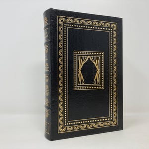 Puede incluir: Un libro encuadernado en cuero negro con detalles dorados y un diseño de cortinas en relieve dorado en la portada.
