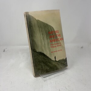 May include: A hardcover book titled "Nature and the American" with a landscape illustration. The cover features a waterfall and a silhouette of a person. The title is in red, with the author's name, Hans Huth, below.