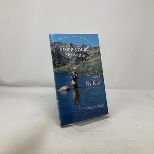 Puede incluir: Un libro titulado "Fishing Small Streams with a Fly Rod" de Charles Meek. La portada presenta una fotografía de una persona pescando con mosca en un río. El agua es azul y el fondo muestra montañas y un cielo azul.
