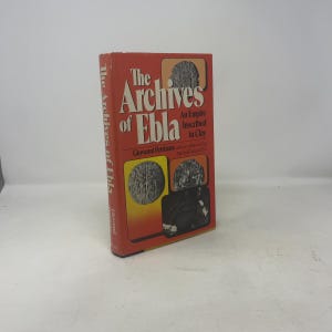 Puede incluir: Un libro de tapa dura rojo titulado "The Archives of Ebla". El libro presenta el título en letras blancas grandes, con el subtítulo "An Empire Inscribed in Clay". La portada también muestra ilustraciones y el nombre del autor.