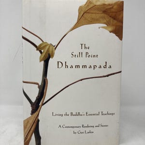 May include: A book titled "The Still Point Dhammapada" with text "Living the Buddha's Essential Teachings" and "A Contemporary Rendering and Stories by Geri Larkin." The cover features a branch with brown leaves.