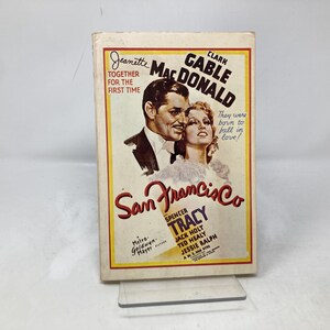 Könnte beinhalten: Ein Vintage-Filmplakat für den Film "San Francisco" mit Clark Gable und Jeanette MacDonald. Das Plakat zeigt ein Schwarzweißbild der beiden Schauspieler, mit dem Titel des Films in rot-weißen Lettern. Das Plakat enthält auch die Namen der Nebendarsteller, darunter Spencer Tracy.