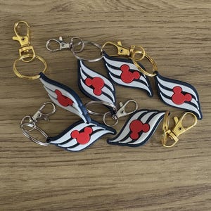 Könnte beinhalten: Schlüsselanhänger mit einem roten Mickey Mouse Kopf-Design auf weißem und schwarz gestreiftem Hintergrund. Die Schlüsselanhänger haben einen goldenen oder silbernen Verschluss und Ring. Die Schlüsselanhänger sind aus Gummi.