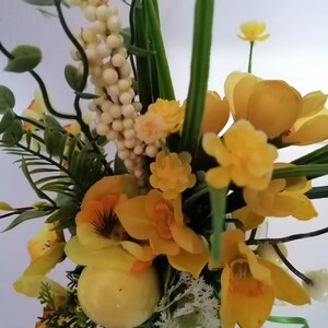 Könnte beinhalten: Eine gelbe Blumenarrangement mit verschiedenen Blumen, darunter Narzissen, und einem einzelnen weißen Ei in der Mitte.