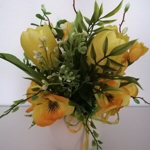 Könnte beinhalten: Eine weiße Keramikvase gefüllt mit einem Strauß gelber und orangefarbener Kunstblumen. Die Blumen umfassen Tulpen, Stiefmütterchen und grüne Zweige.