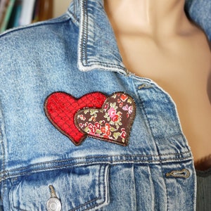May include: A denim jacket with two fabric hearts sewn on the front. The hearts are red and brown with a floral pattern.