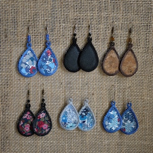 Peut inclure: Collection de boucles d'oreilles en forme de goutte d'eau avec différents motifs. Styles incluent des motifs floraux bleus et rouges, du cuir noir uni et du liège. Chaque paire a un crochet en métal, sur un fond texturé neutre.