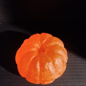 May include: A bright orange, segmented object resembling a tangerine or clementine. The object is round with a central indentation and a textured surface. The background is a solid black.