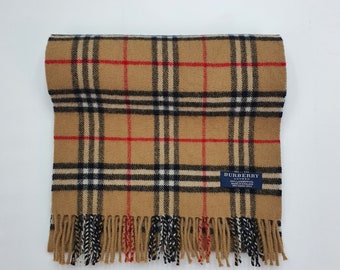 Op de afbeelding: Een bruine en beige geruite sjaal met zwarte, witte en rode strepen. De sjaal heeft franjes aan de uiteinden en een blauw label met de tekst "Burberry London" en "100% Kasjmier Gemaakt in Engeland".