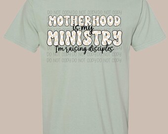 May include: A light green t-shirt with the text "MOTHERHOOD is my MINISTRY I'm raising disciples" in a playful font. The shirt is a solid color and has short sleeves.