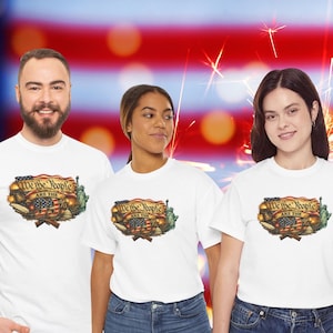 May include: Three people wearing white t-shirts with a patriotic design. The shirts feature the text "We the People ARE THE %" above an American flag, the Statue of Liberty, and crossed rifles. They are wearing blue jeans.