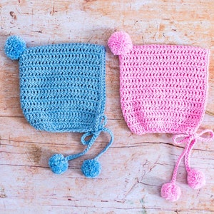 May include: Two crocheted baby hats with pom-poms. One hat is light blue and the other is pink.