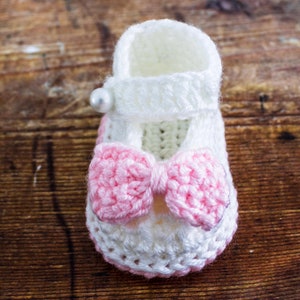 May include: White crocheted baby booties with a pink bow and a pearl embellishment.