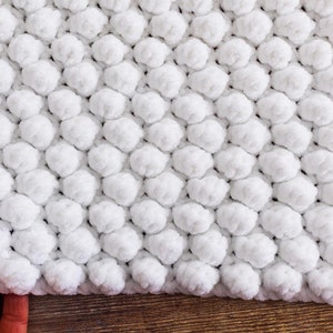 May include: White crocheted blanket with a textured, puffy design. The blanket is made with a soft, fluffy yarn.