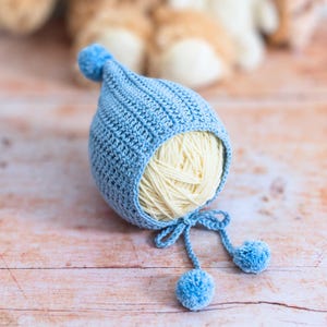 May include: A light blue crocheted baby hat with white yarn inside and two blue pom-poms.