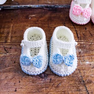 May include: Two pairs of crocheted baby booties with bows. One pair is white with blue bows and the other pair is white with pink bows.