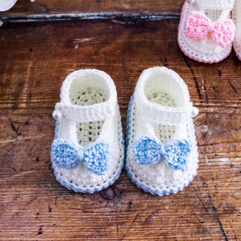 May include: Two pairs of crocheted baby booties with bows. One pair is white with blue bows and the other pair is white with pink bows.