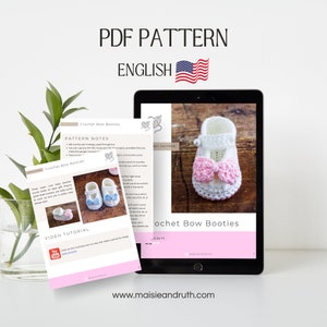 May include: A digital PDF pattern for crocheting baby booties with a bow. The pattern is in English and includes a video tutorial. The booties are white with a pink bow and are shown on a tablet.