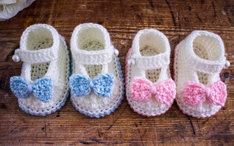 May include: Four pairs of crocheted baby booties with bows. Two pairs have blue bows and two pairs have pink bows.