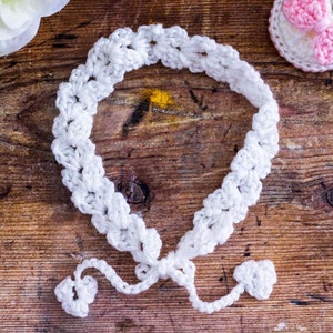 May include: White crocheted headband with a tied bow on a wooden background.