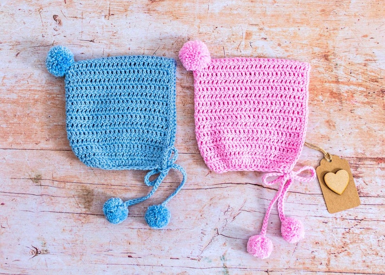 May include: Two crocheted baby hats with pom-poms. One hat is light blue and the other is pink.